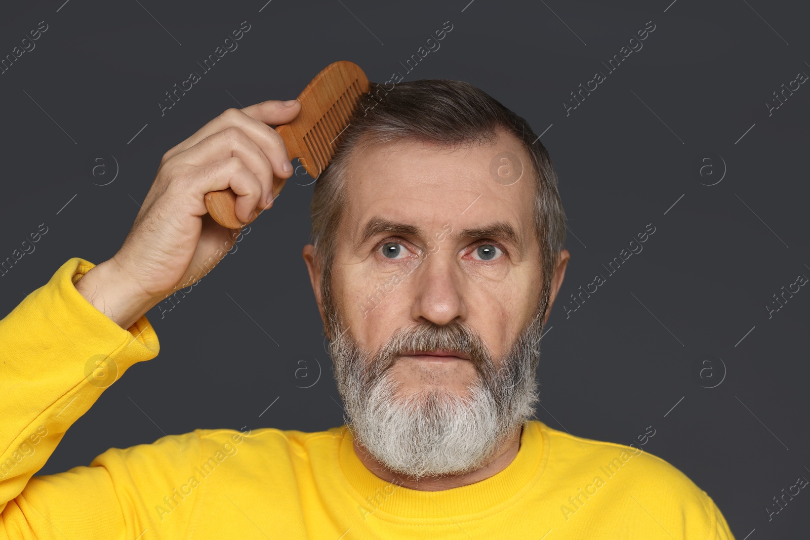 Photo of Handsome man combing his hair on dark grey background