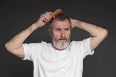 Photo of Handsome man combing his hair on dark grey background