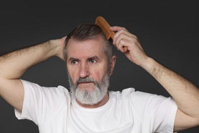 Photo of Handsome man combing his hair on dark grey background