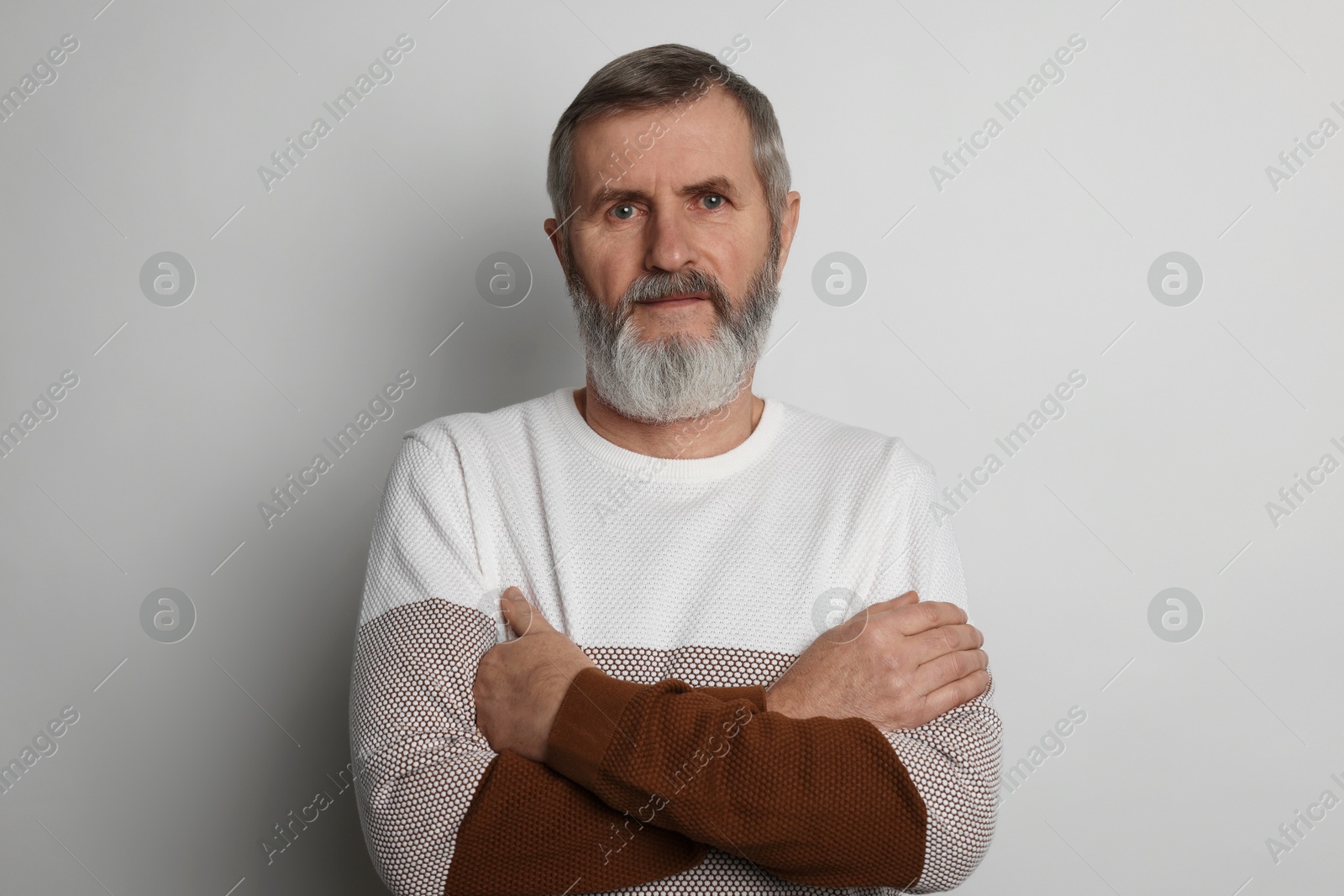 Photo of Portrait of mature man with crossed arms on light grey background