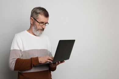 Photo of Mature man with laptop on light grey background, space for text