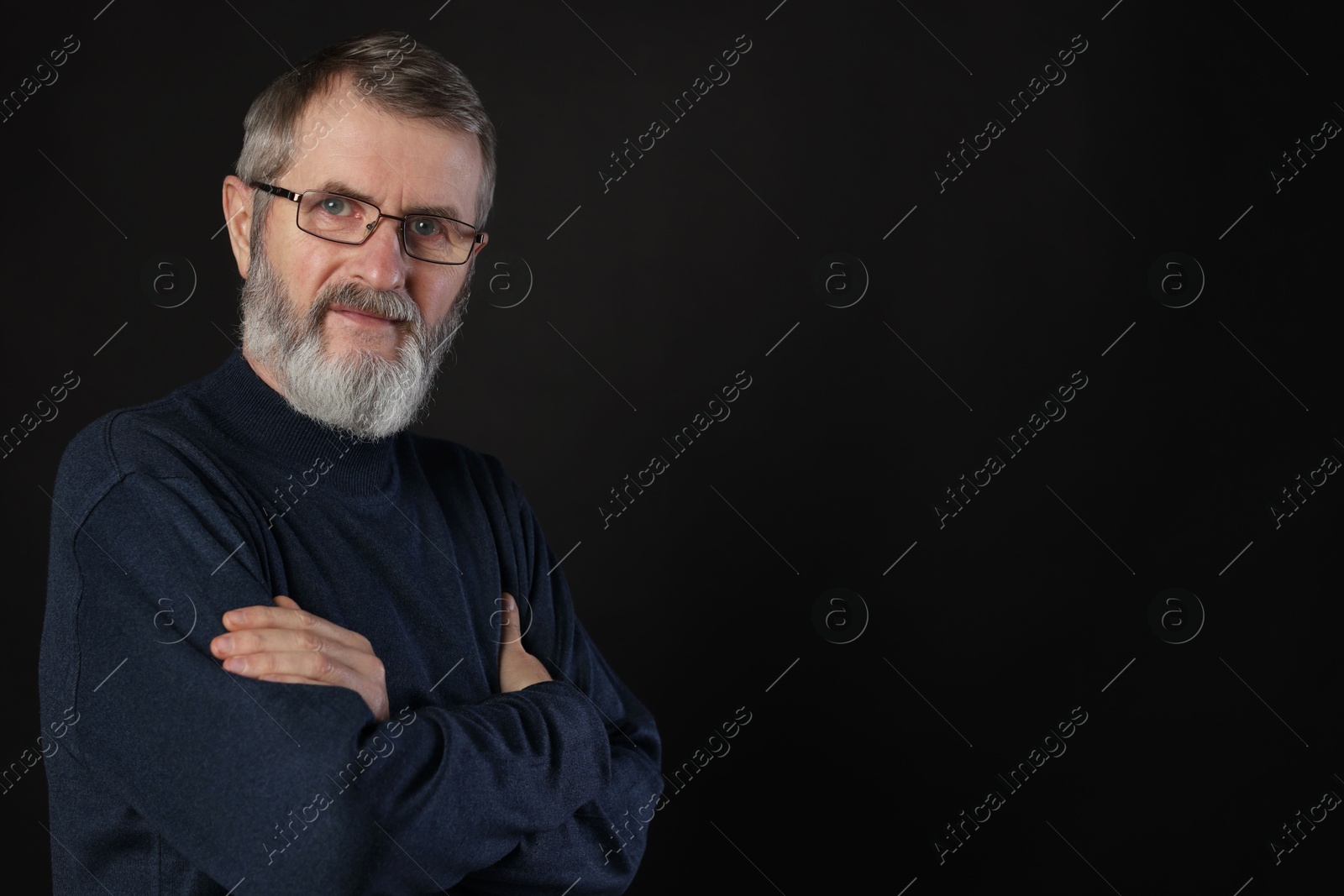 Photo of Portrait of mature man with crossed arms on black background, space for text