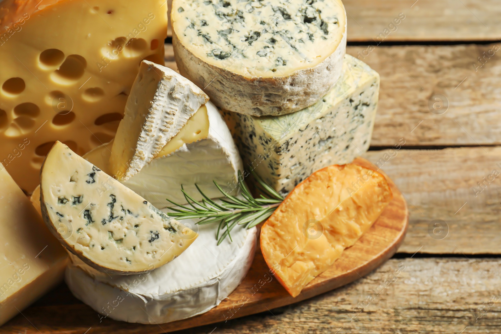 Photo of Different types of cheese and rosemary on wooden table, closeup