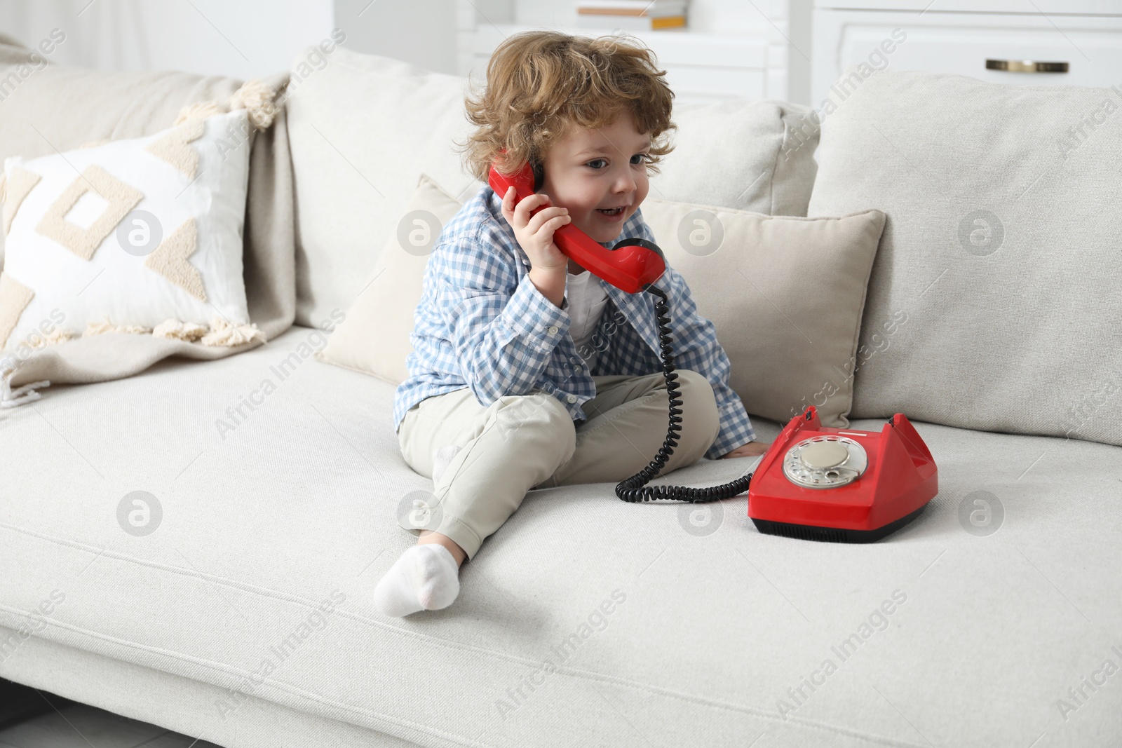 Photo of Cute little boy with telephone on sofa indoors