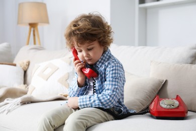 Photo of Cute little boy with telephone on sofa indoors