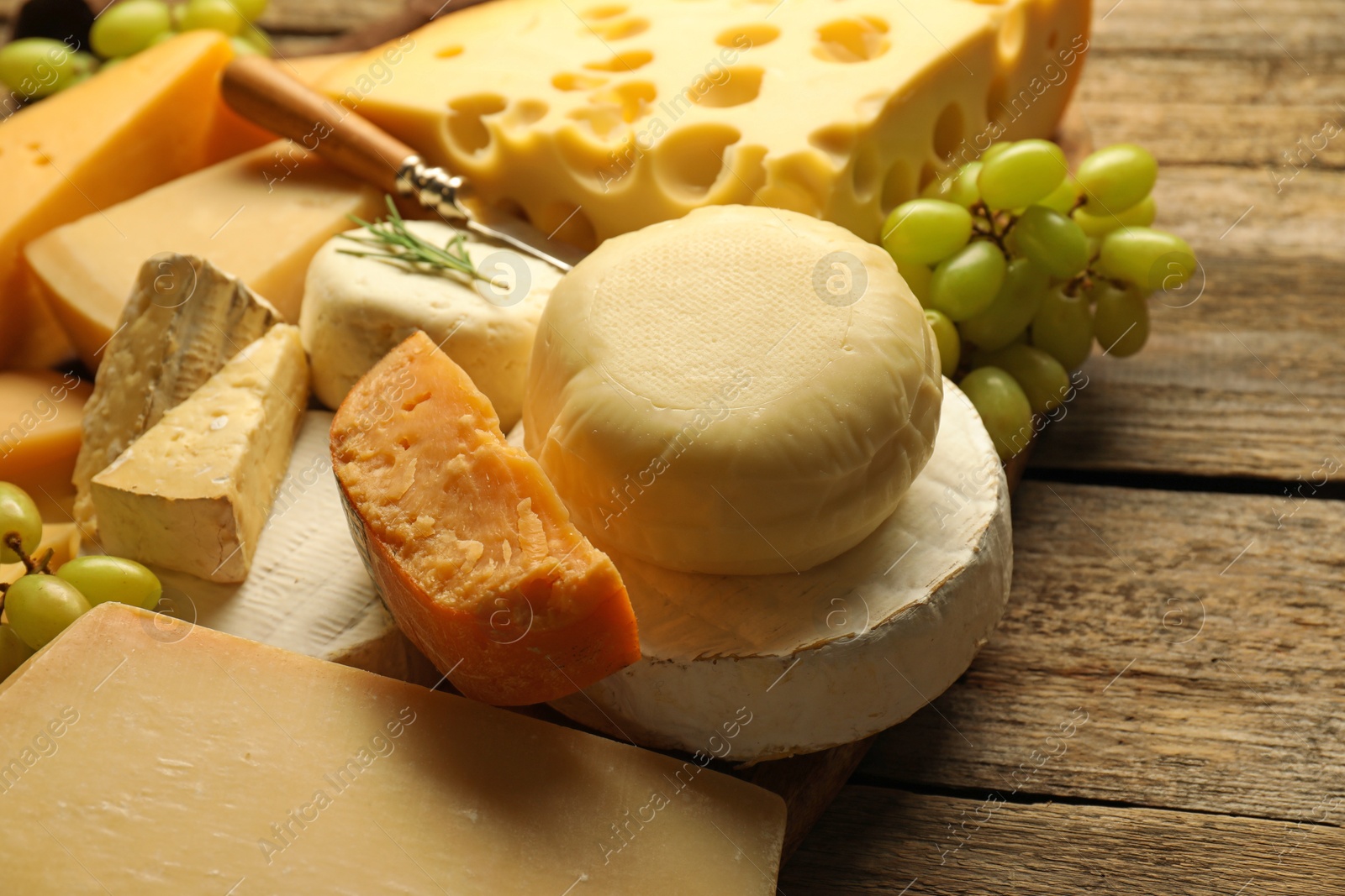 Photo of Different types of cheese and grapes on wooden table, closeup