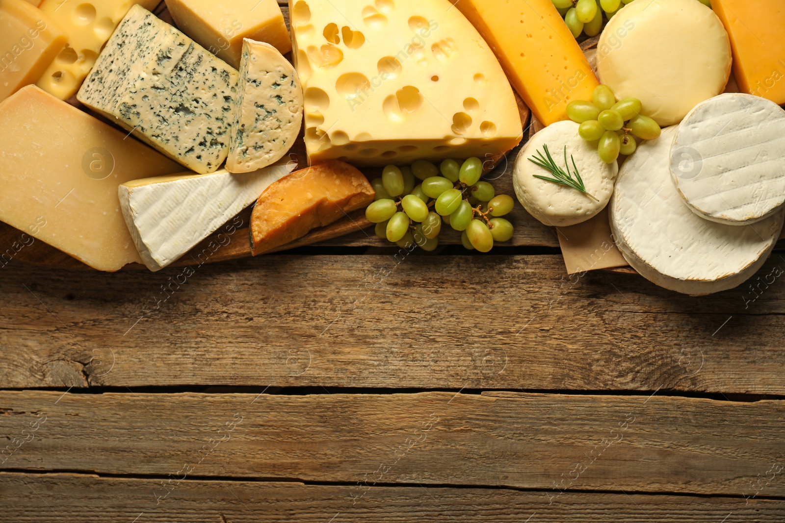 Photo of Different types of cheese, rosemary and grapes on wooden table, flat lay. Space for text