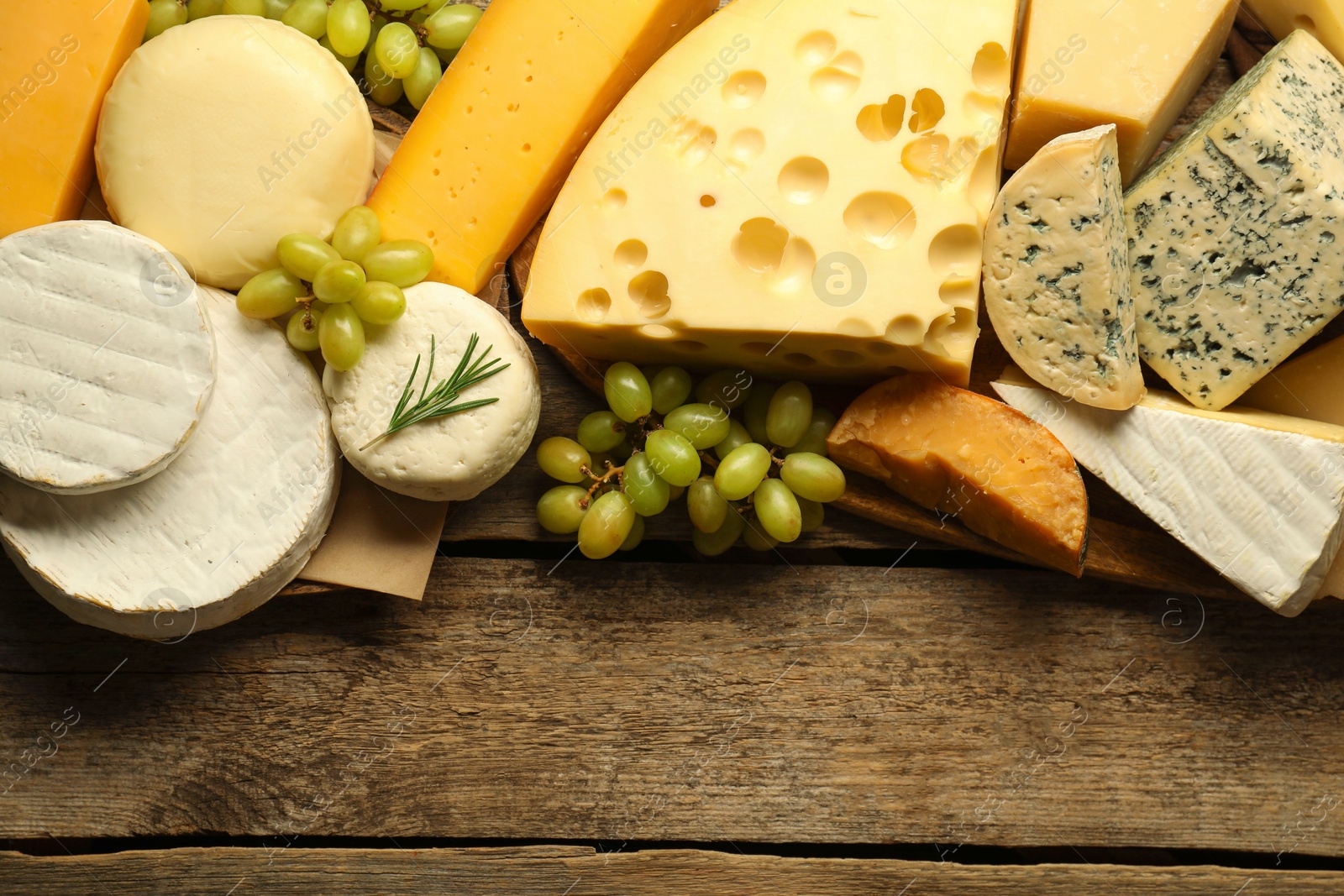 Photo of Different types of cheese, rosemary and grapes on wooden table, flat lay. Space for text