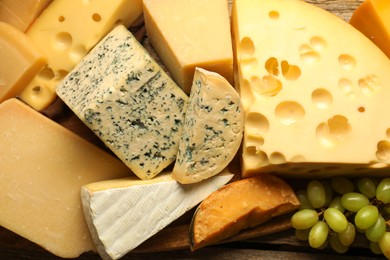 Photo of Different types of cheese and grapes on wooden table, flat lay