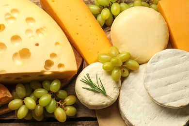 Photo of Different types of cheese, rosemary and grapes on wooden table, flat lay