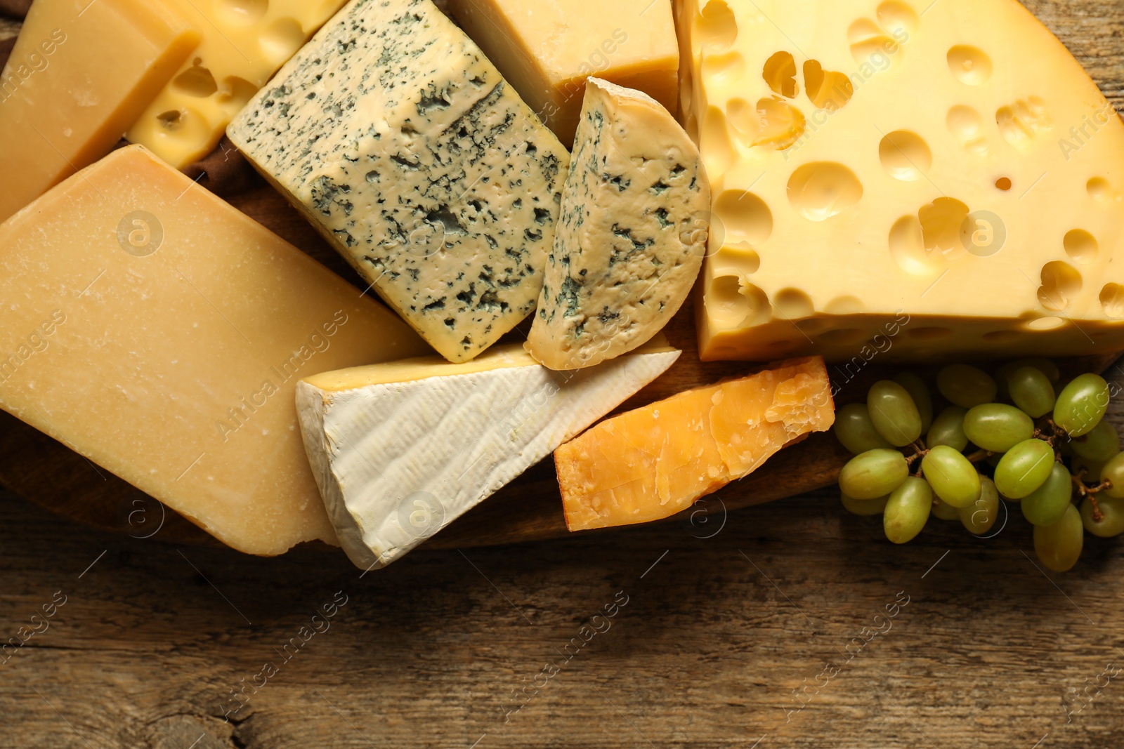 Photo of Different types of cheese and grapes on wooden table, flat lay