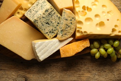 Photo of Different types of cheese and grapes on wooden table, flat lay