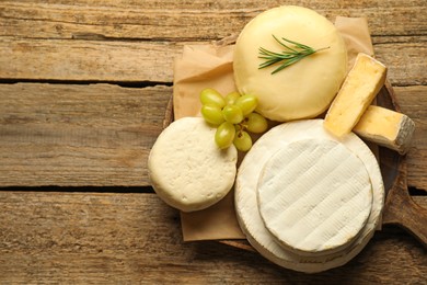 Photo of Different types of cheese, rosemary and grapes on wooden table, top view. Space for text