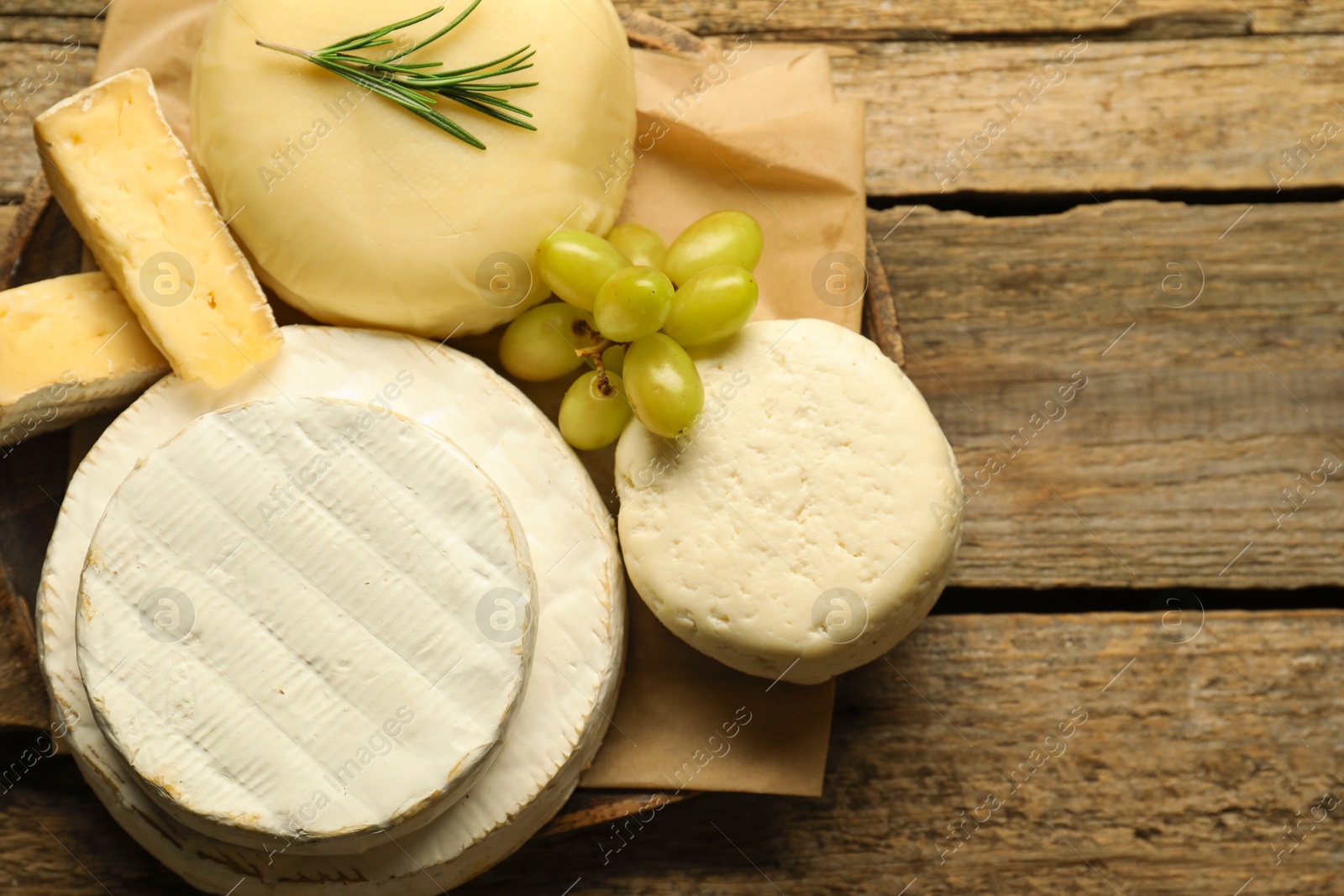 Photo of Different types of cheese, rosemary and grapes on wooden table, top view. Space for text