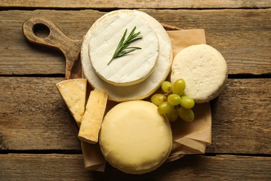 Photo of Different types of cheese, rosemary and grapes on wooden table, top view