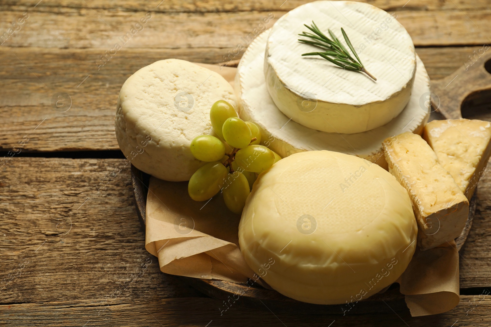 Photo of Different types of cheese, rosemary and grapes on wooden table, closeup