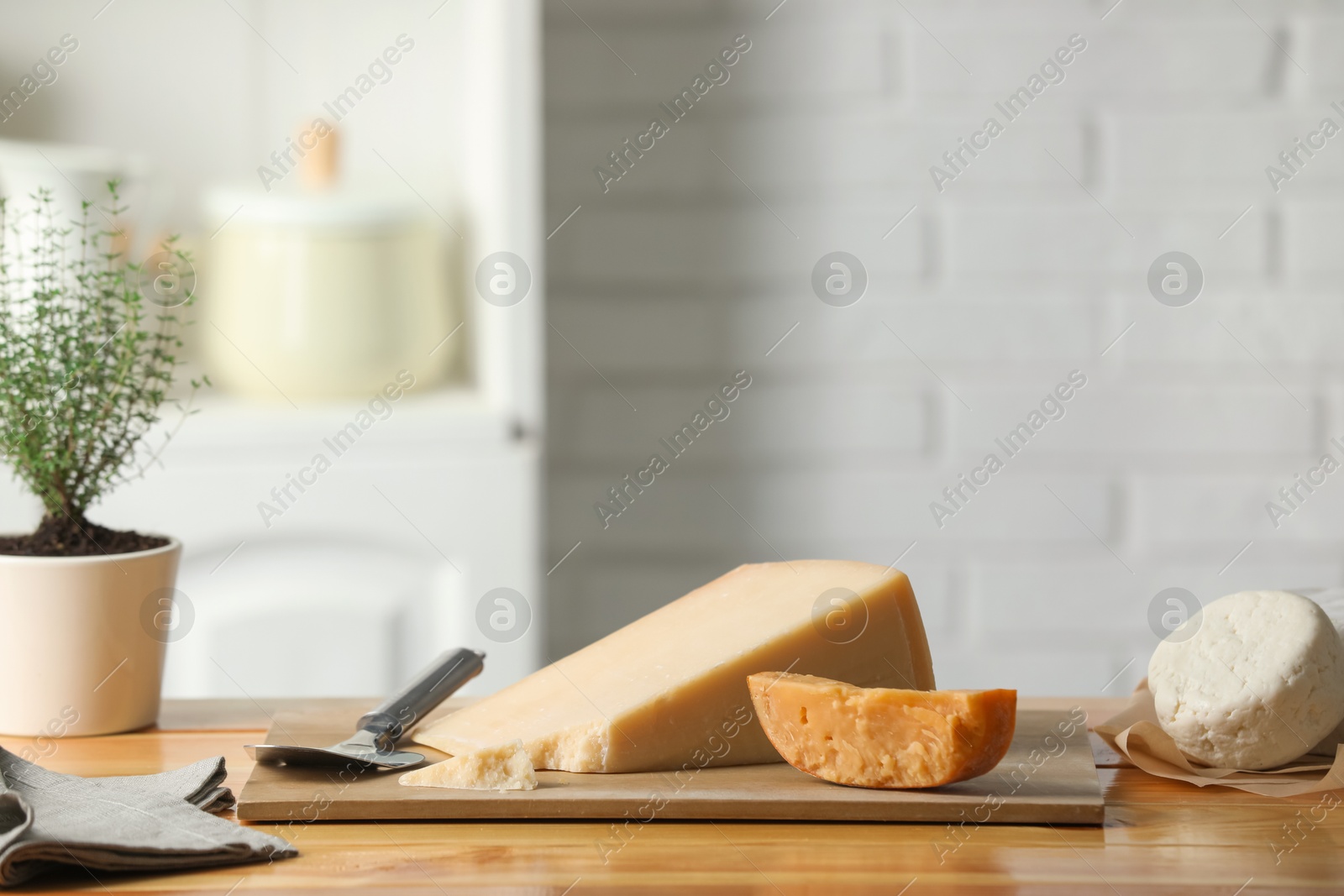 Photo of Different types of cheese, slicer and potted thyme on wooden table indoors. Space for text