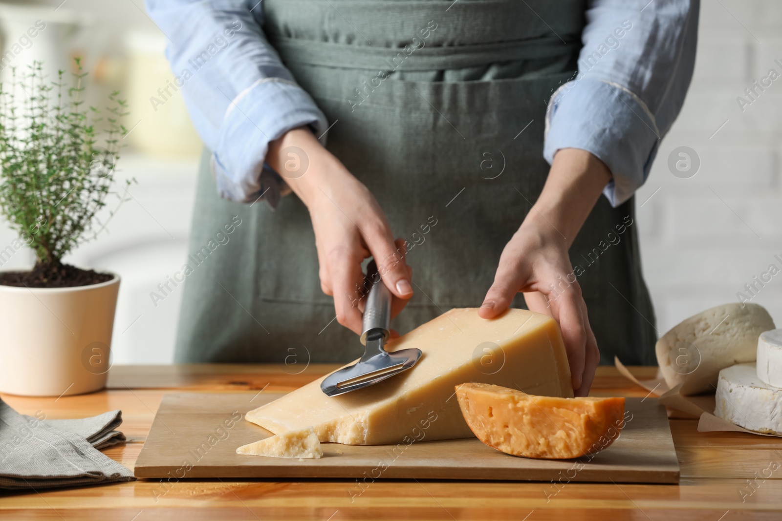 Photo of Woman cutting delicious cheese with slicer at wooden table indoors, closeup