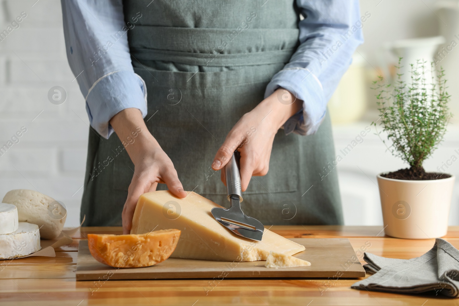 Photo of Woman cutting delicious cheese with slicer at wooden table indoors, closeup