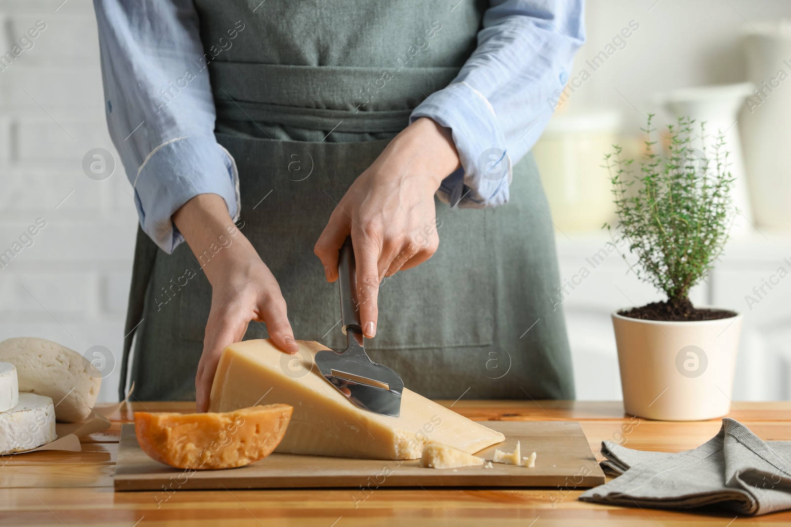 Photo of Woman cutting delicious cheese with slicer at wooden table indoors, closeup