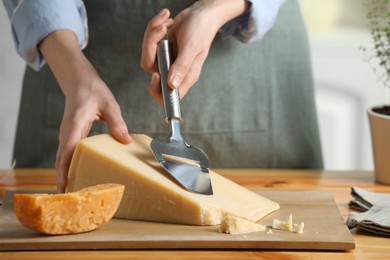 Photo of Woman cutting delicious cheese with slicer at wooden table indoors, closeup