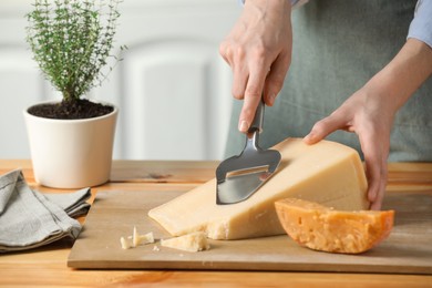 Photo of Woman cutting delicious cheese with slicer at wooden table indoors, closeup