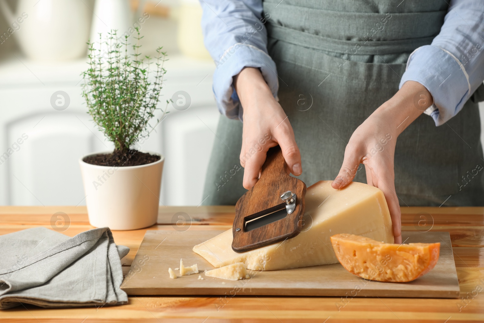 Photo of Woman cutting delicious cheese with slicer at wooden table indoors, closeup