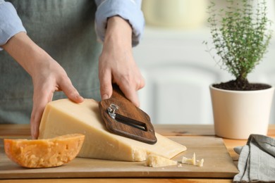 Photo of Woman cutting delicious cheese with slicer at wooden table indoors, closeup