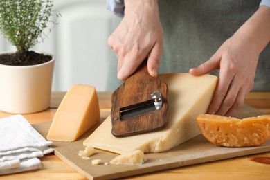 Photo of Woman cutting delicious cheese with slicer at wooden table indoors, closeup