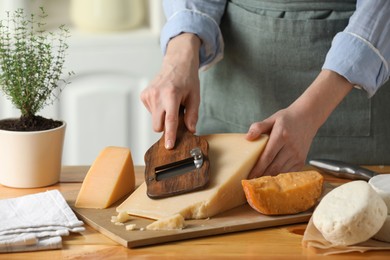 Photo of Woman cutting delicious cheese with slicer at wooden table indoors, closeup