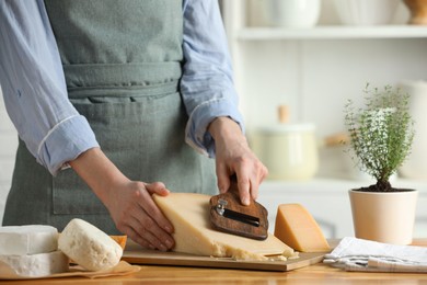 Photo of Woman cutting delicious cheese with slicer at wooden table indoors, closeup