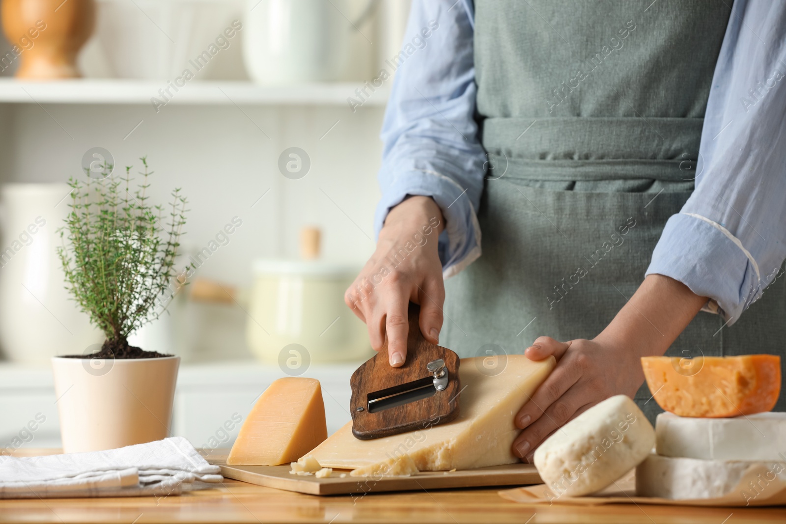 Photo of Woman cutting delicious cheese with slicer at wooden table indoors, closeup