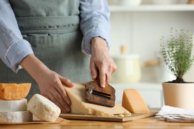 Photo of Woman cutting delicious cheese with slicer at wooden table indoors, closeup