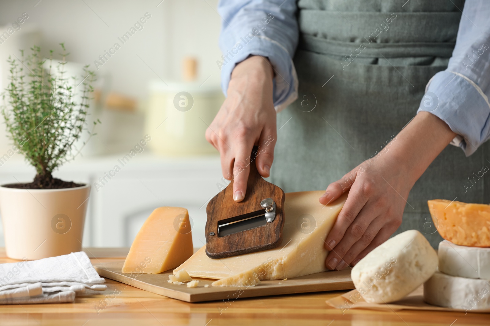 Photo of Woman cutting delicious cheese with slicer at wooden table indoors, closeup