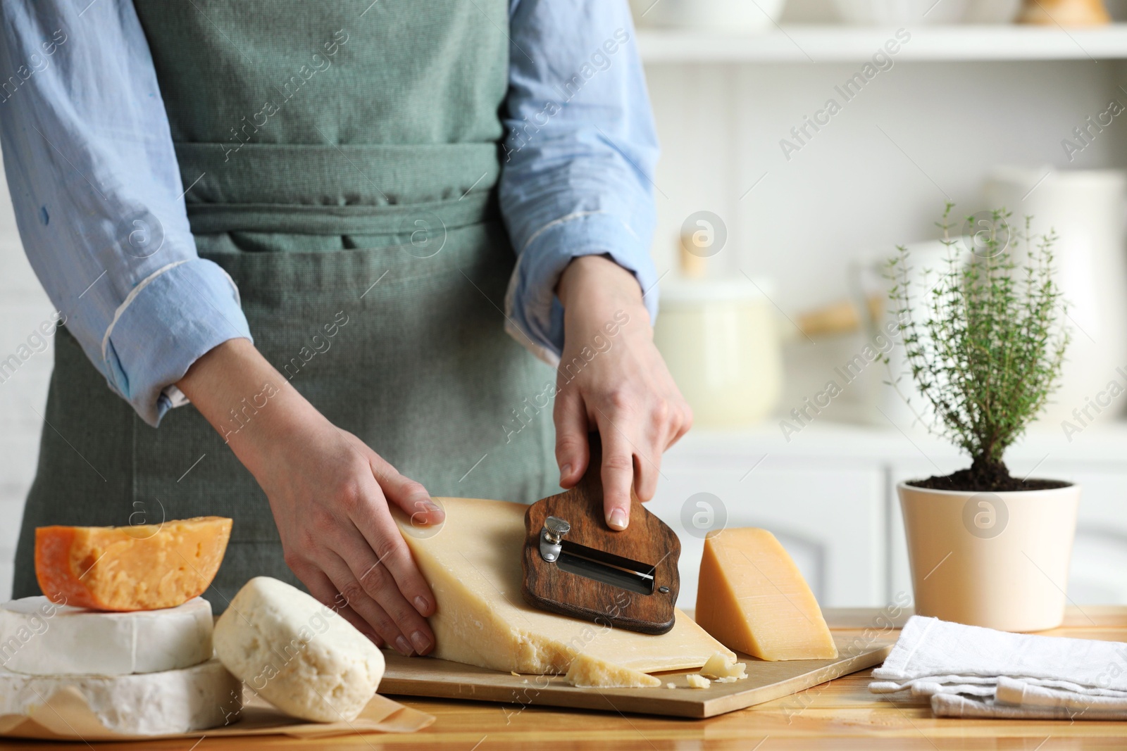 Photo of Woman cutting delicious cheese with slicer at wooden table indoors, closeup