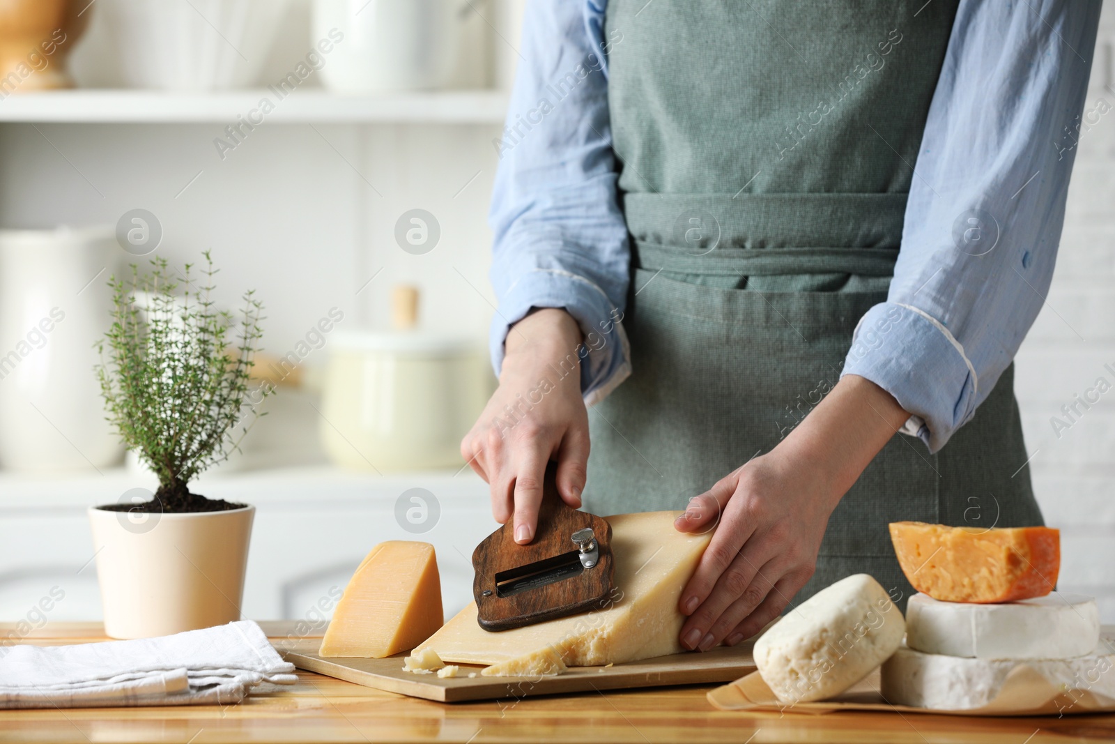 Photo of Woman cutting delicious cheese with slicer at wooden table indoors, closeup