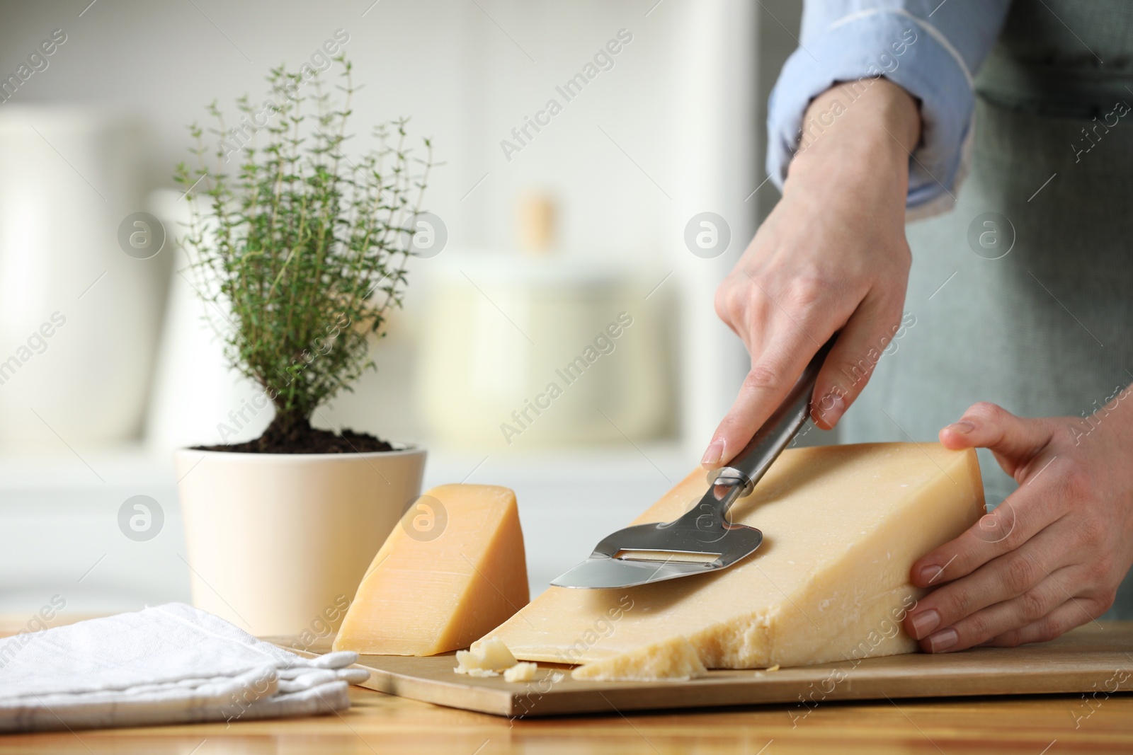 Photo of Woman cutting delicious cheese with slicer at wooden table indoors, closeup