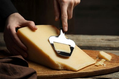 Photo of Woman cutting delicious cheese with slicer at wooden table against black background, closeup