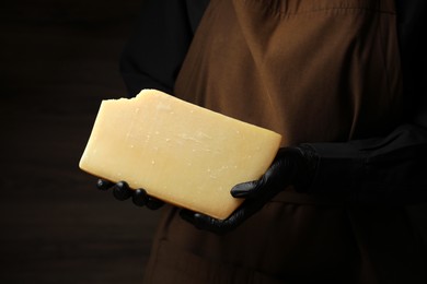 Photo of Woman with piece of delicious cheese on black background, closeup