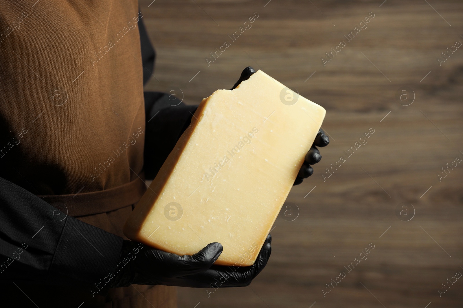 Photo of Woman with piece of delicious cheese on wooden background, closeup. Space for text