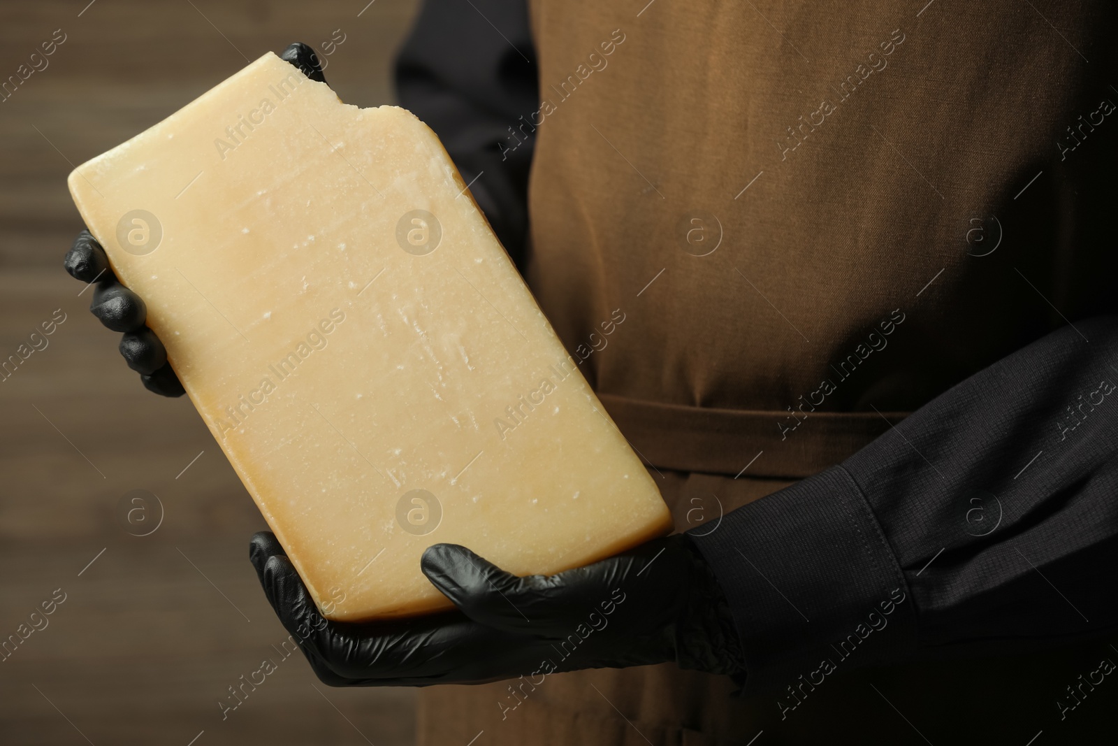 Photo of Woman with piece of delicious cheese on wooden background, closeup