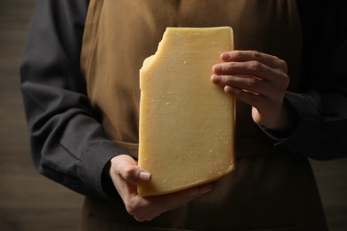 Photo of Woman with piece of delicious cheese on wooden background, closeup