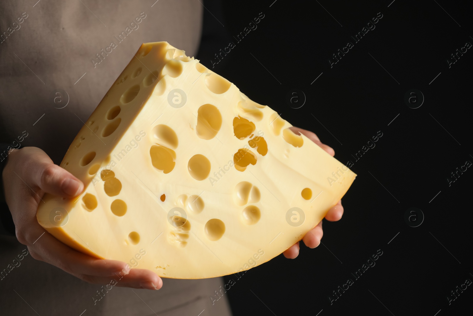 Photo of Woman with piece of delicious cheese on black background, closeup