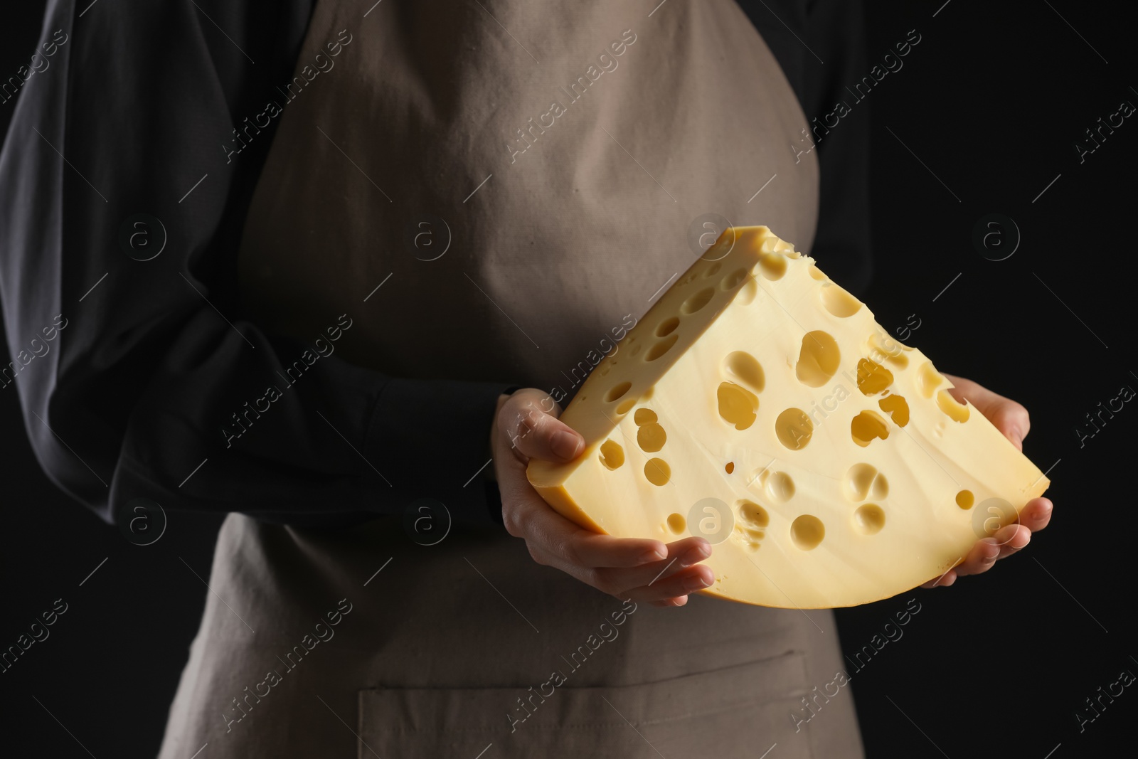 Photo of Woman with piece of delicious cheese on black background, closeup