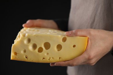 Photo of Woman with piece of delicious cheese on black background, closeup