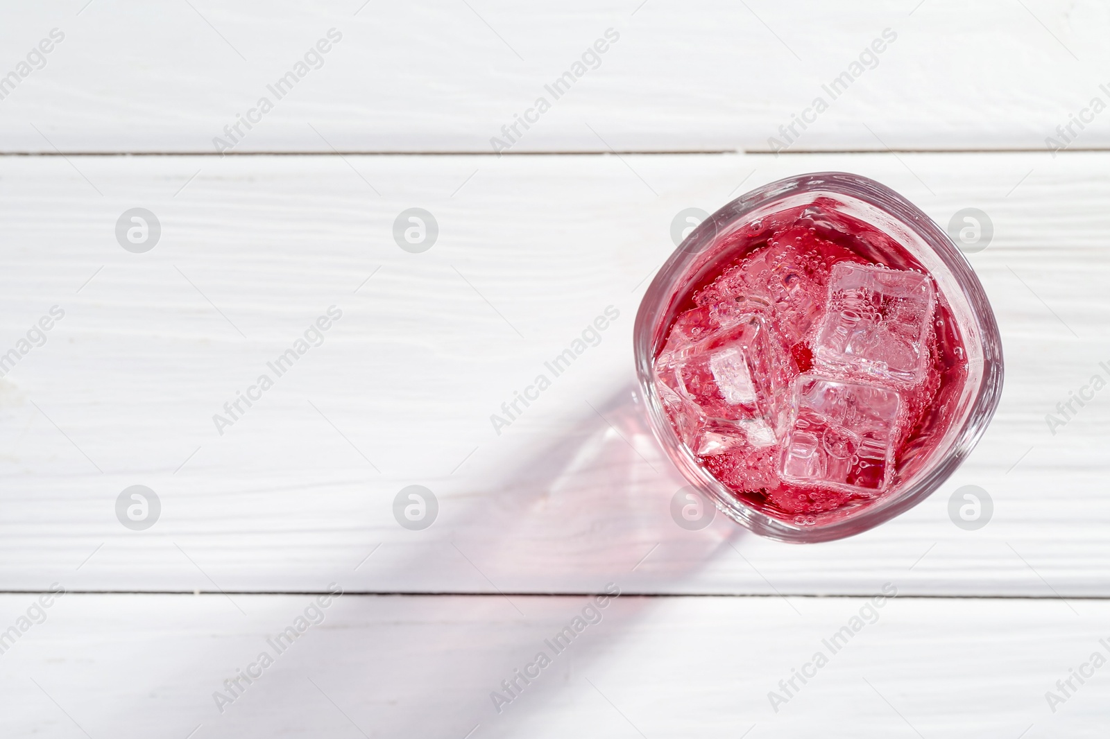 Photo of Sweet soda water with ice cubes in glass on white wooden table, top view. Space for text