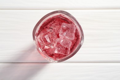 Photo of Sweet soda water with ice cubes in glass on white wooden table, top view