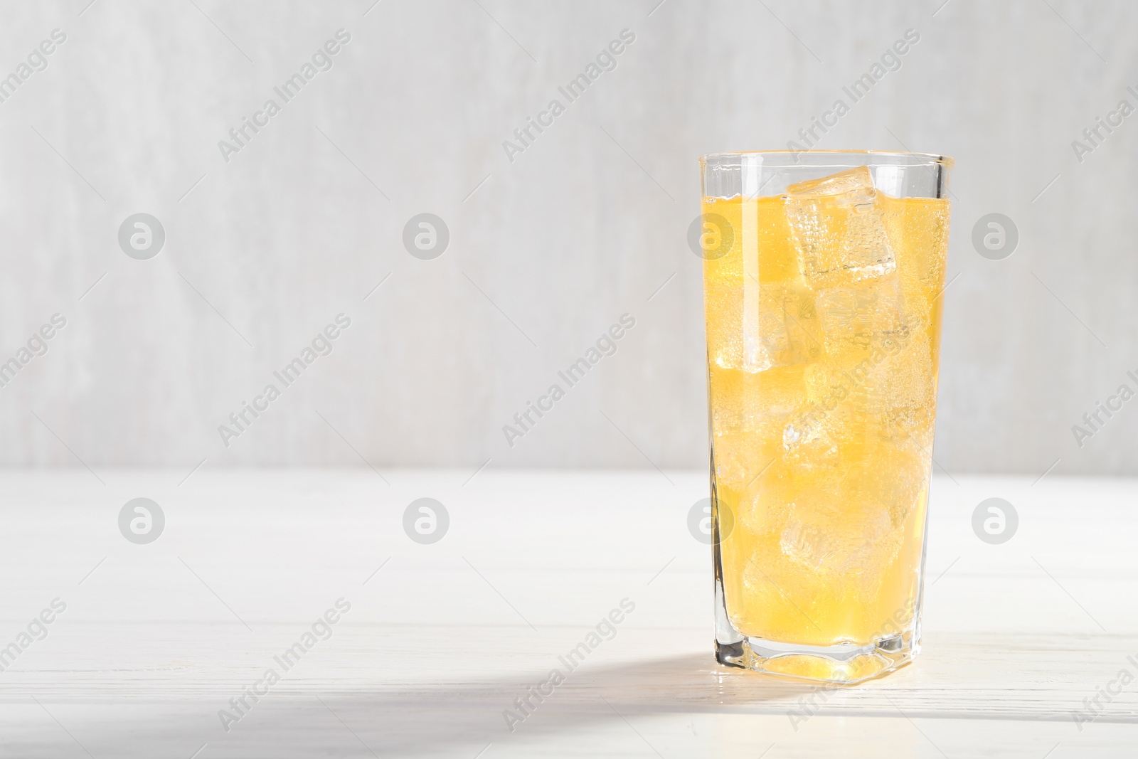 Photo of Sweet soda water with ice cubes in glass on white wooden table, space for text