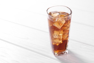 Photo of Sweet soda water with ice cubes in glass on white wooden table, space for text