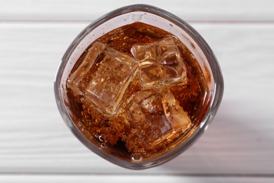 Photo of Sweet soda water with ice cubes in glass on white wooden table, top view